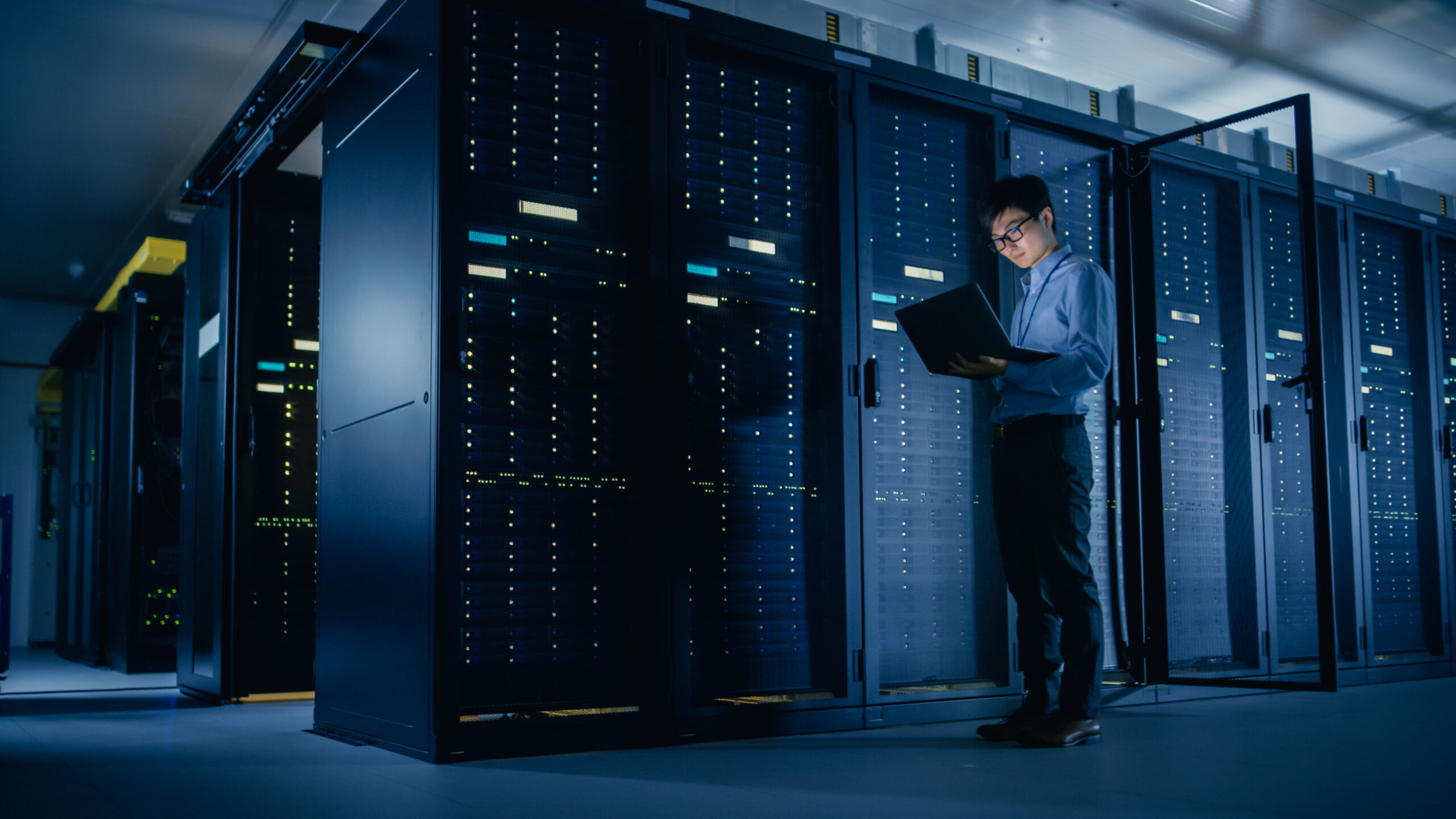 An image of an IT worker looking at her laptop in a darkened data center.