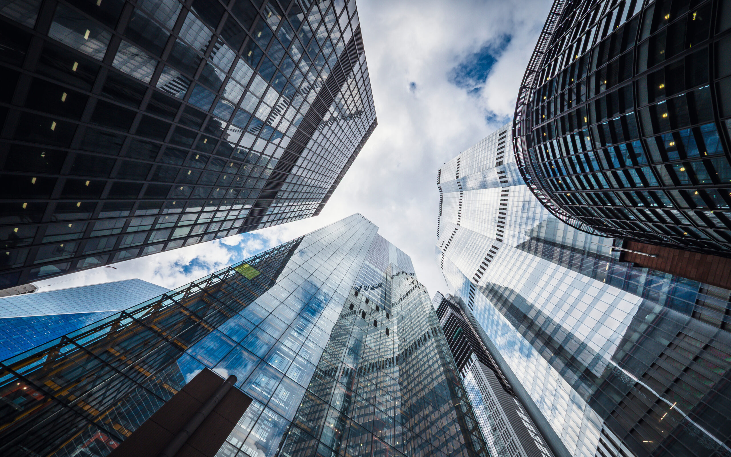 A view looking toward the sky between towering skyscrapers of glass and steel.